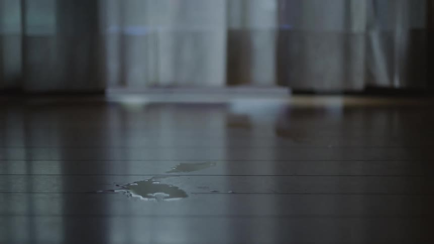 Small puddle of spilled water sits on wooden floor near blowing curtain