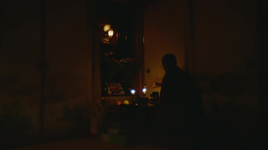 Man kneeling in front of a shrine extinguishes a couple candles