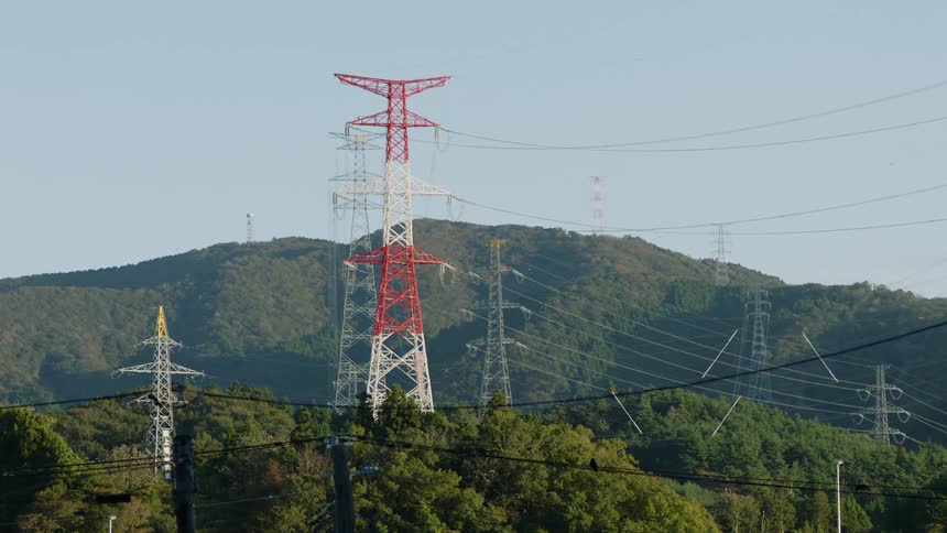 Cables connecting transmission towers high above the trees with mountains in the distance under a clear sky