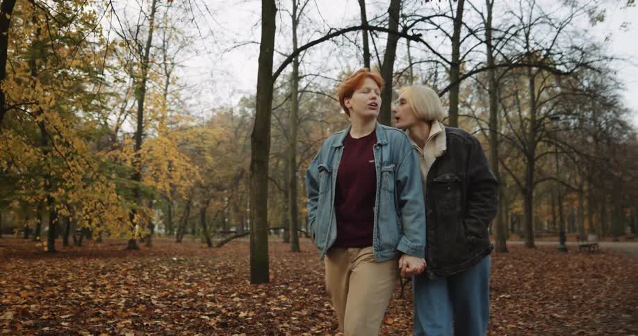 Lesbian couple wearing denim jackets shirts and pants walks in the forest with brown leaves