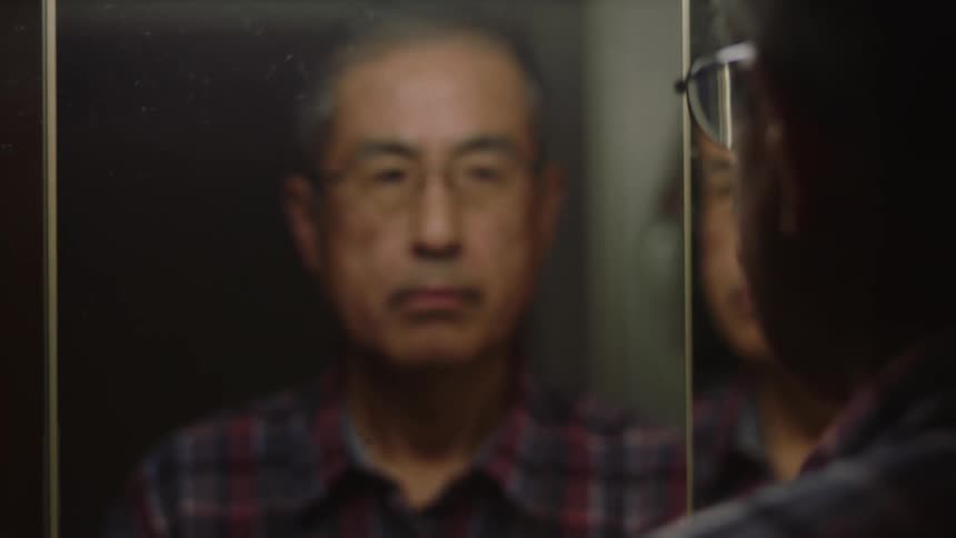 Man stands facing his reflection in a multi paneled mirrored surface