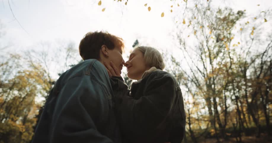 A woman is walking down a ledge next to stairs and when she gets to the bottom she hugs and kisses a woman and they hold hands as they walk up the stairs together