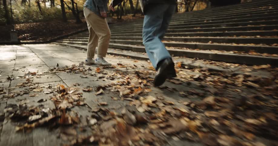 Two women are kicking leaves at each other and playing on the steps in a park with trees in fall colors