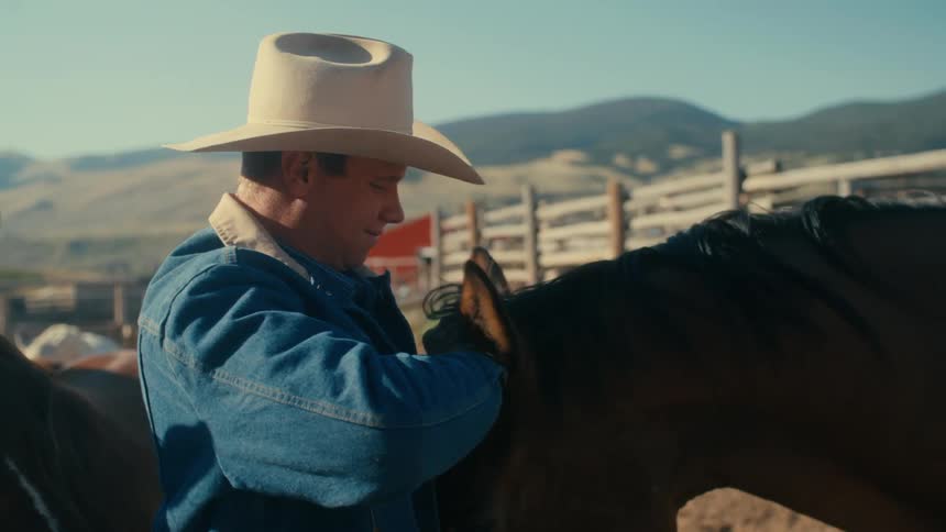 A man is standing at his ranch with his horse