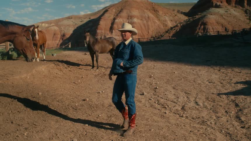 A man shakes his hand in his pocket as he talks to horses in a pasture