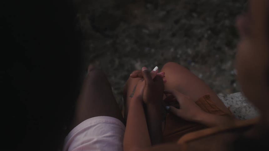 A young couple is holding hands and sitting down outside
