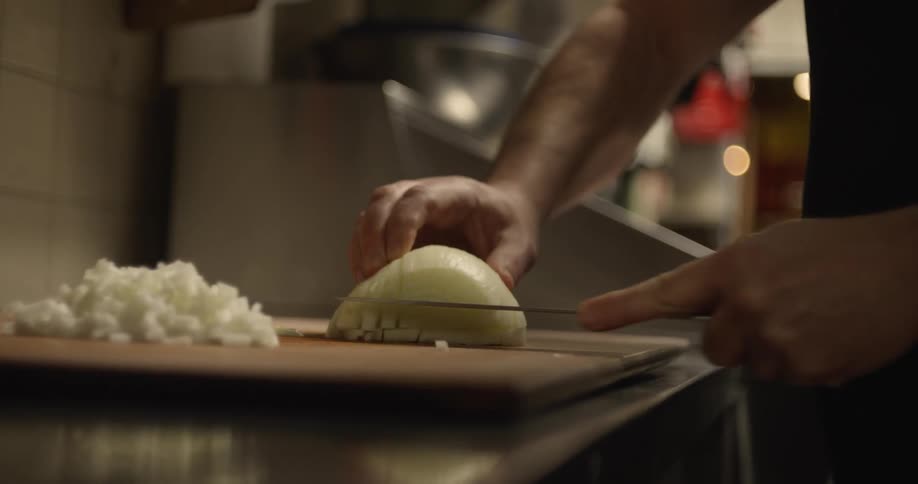 Man chopping onions rapidly in a restaurant kitchen