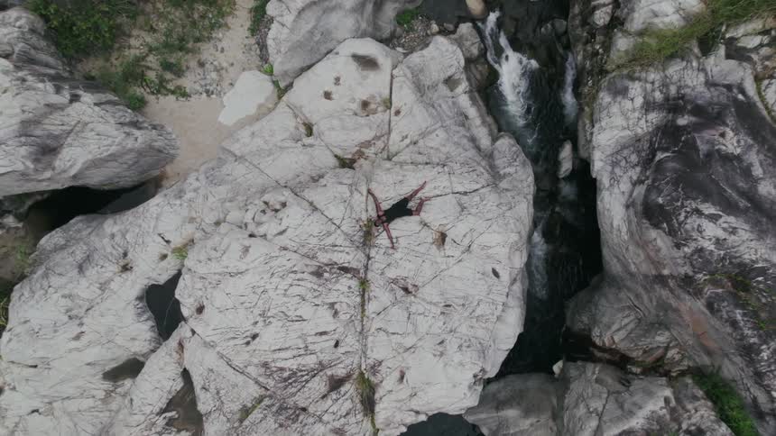 Aerial zoom top of a rock next to a flowing waterfall in the wilderness