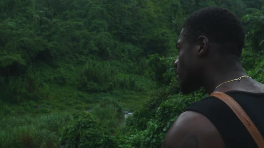 The view is of a young black man that is in the forest