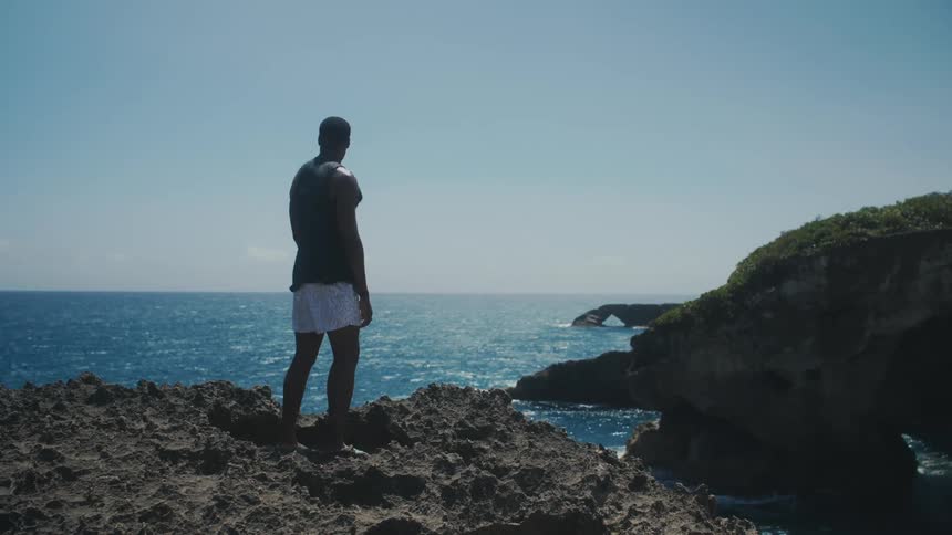 A young man is standing on a cliff and is looking at the ocean