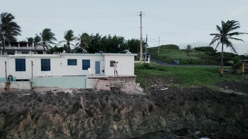 Man stands on patio of ocean side homeas car turns at nearby intersection