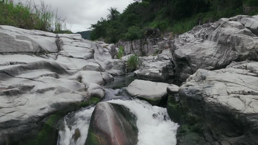 Water in a stream at the foot of a mountain rushes over rocks as it rapidly flows downward