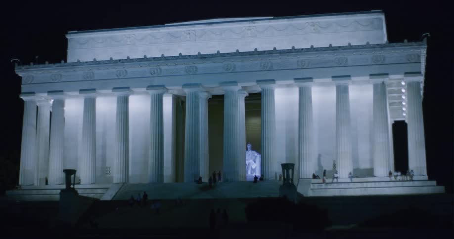 There are people walking outside at night by this monument