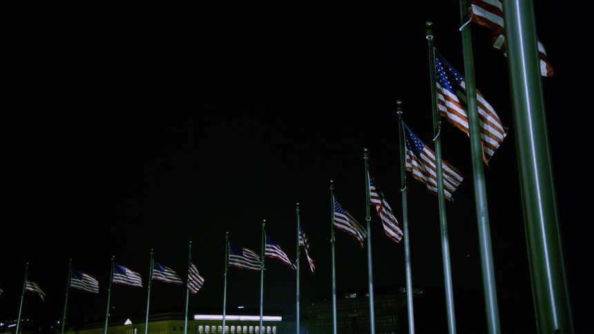 American flags wave atop a role of flagpoles at night