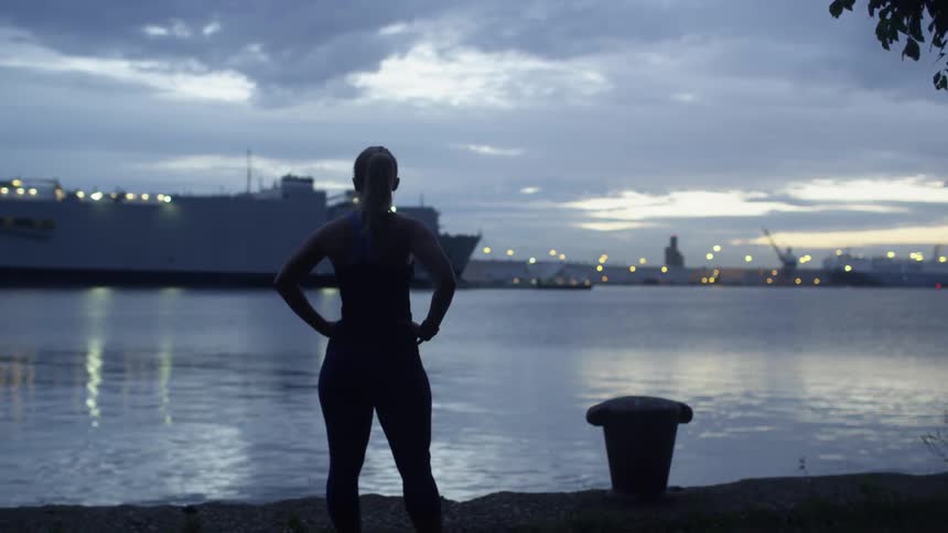 A woman stands by the water at sunset