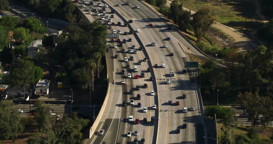 Traffic on a busy highway travels around a curve as cars below move through a neighborhood