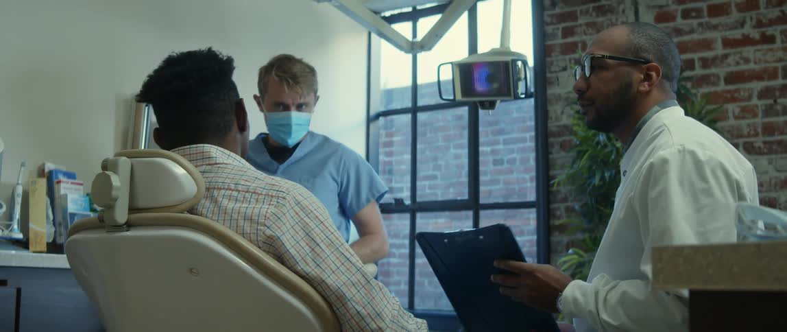 Patient sitting on a dentist chair talking to a nurse and doctor