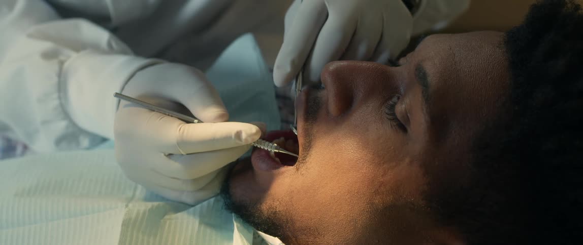 There is a black man that is at the dentist cleaning his teeth