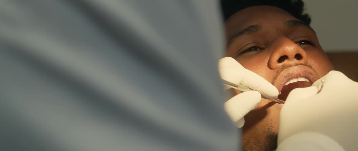 Dentist wearing gloves treats patient using mouth mirror at clinic