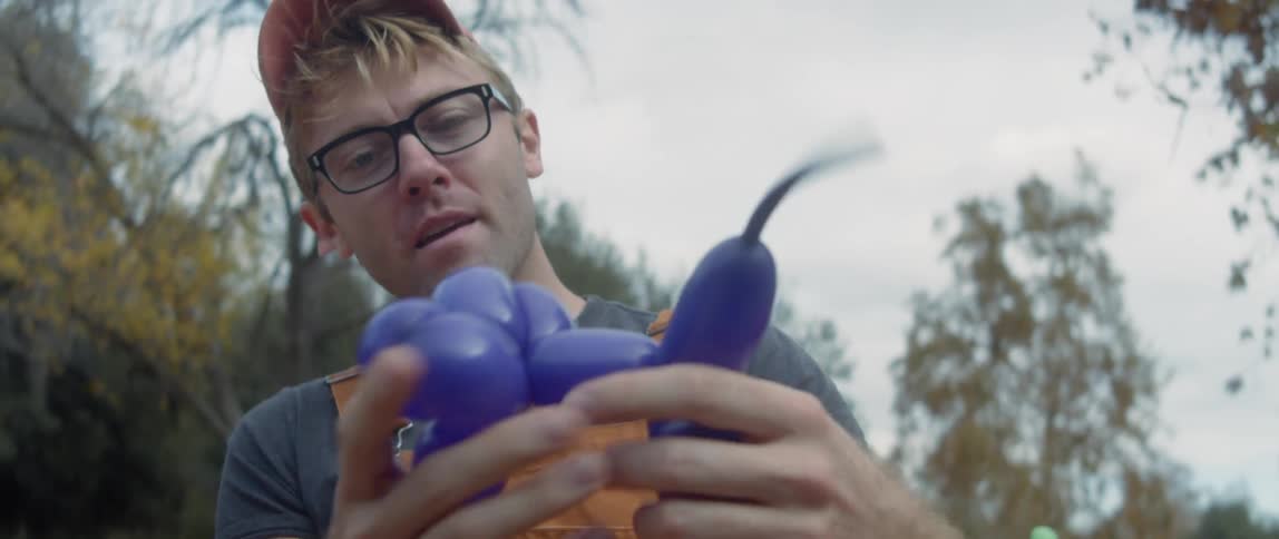 Man wearing overalls makes balloon animals for a party in the park