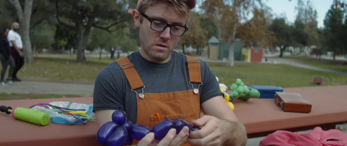 A male is making balloons and sitting at a park