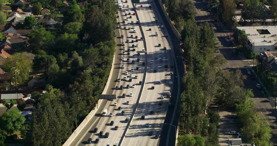 An aerial view of cars driving on a freeway with businesses on one side and houses on the other