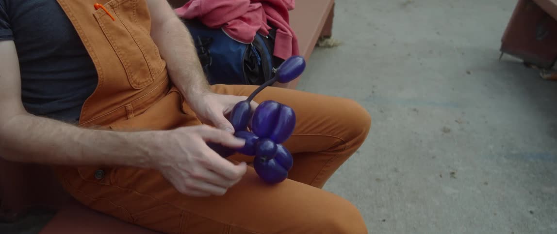 Man sits outdoors on bench working with balloon art