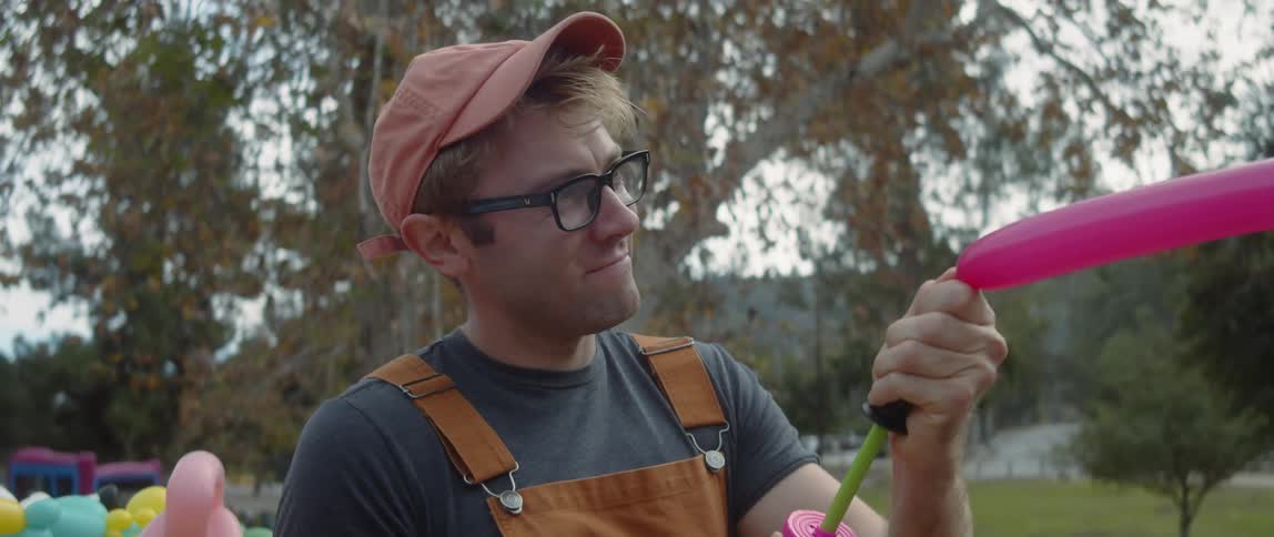 Male balloon artist fills balloons with air pump while sitting in park
