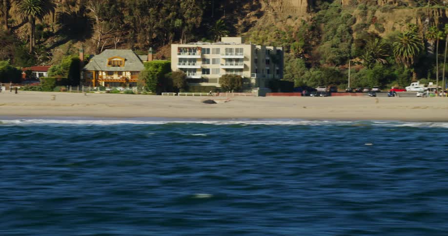 A person rides a bike along a beach lined with houses and hotels as vehicles drive in the distance