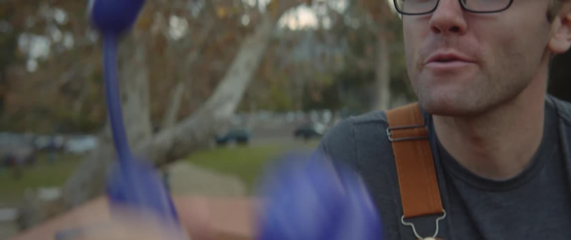 Man wearing overalls makes balloon animals for a party in the park