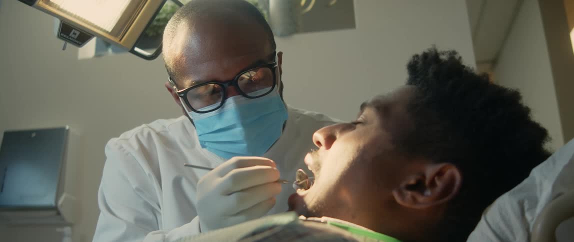 Dentist with glasses mask and white shirt treats patient at clinic