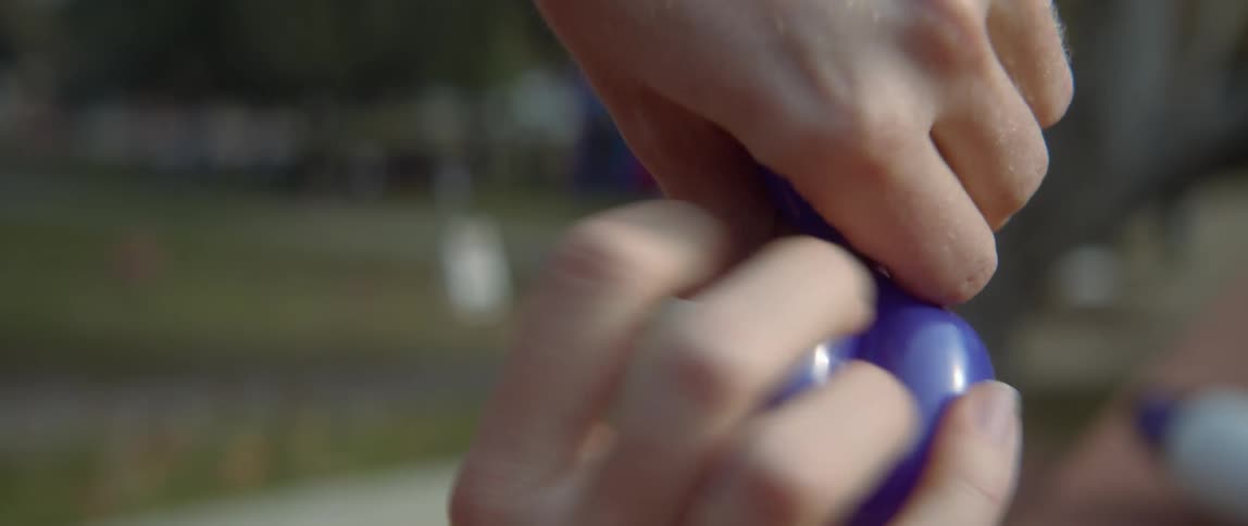 Someone is outside twisting a blue balloon into an animal with their hands