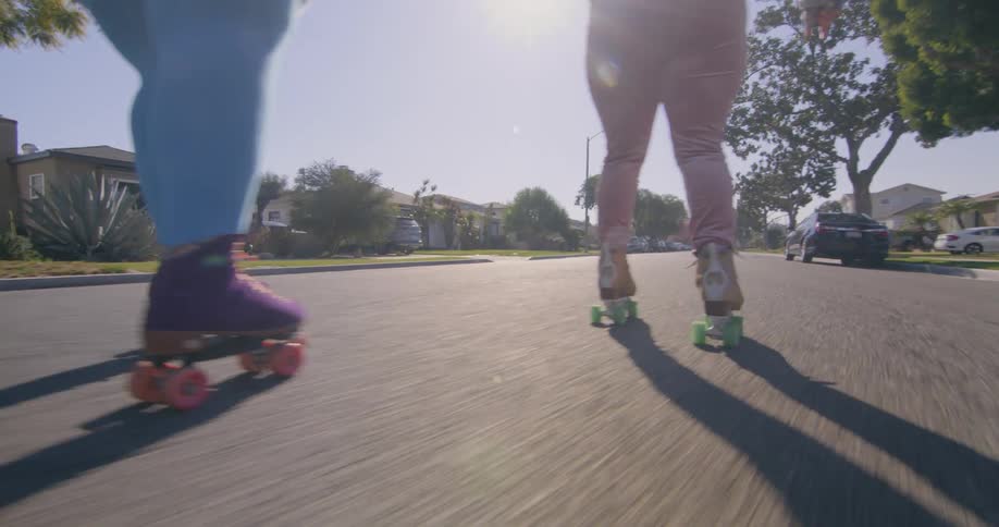 Two women hold hands as they roller skate down a neighborhood street
