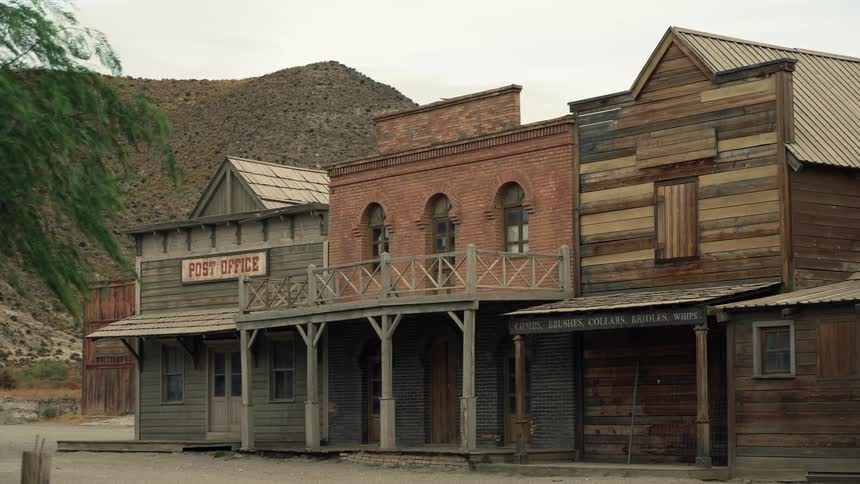 An old western post office made out of wooden planks sits at the foot of a desert hill