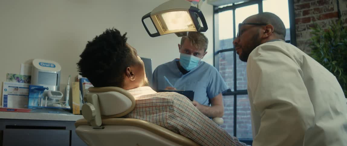 Dentist and nurse checks a patient with his mouth open reclined on a chair
