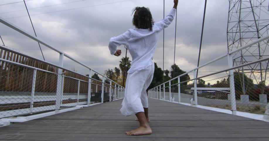 A person is dancing on a bridge at dusk