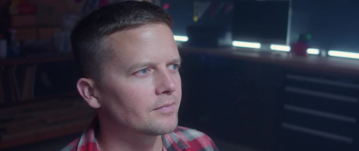 A man is sitting in a room with lights on a table behind him as he nods his head