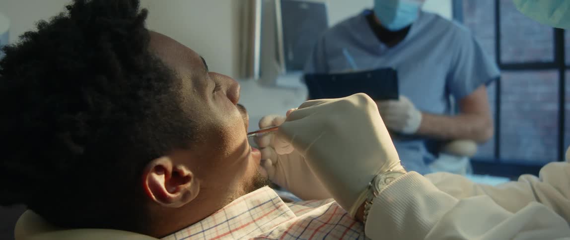 A dentist uses a dental mirror to examine the mouth of a patient as a nurse takes notes