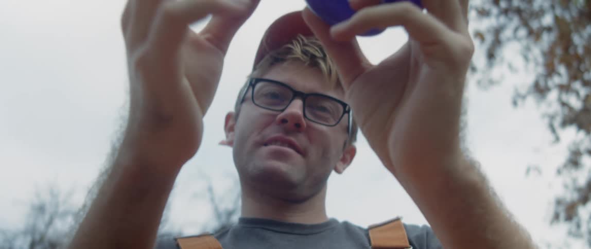 A man wearing glasses attempts to twist a balloon into the shape of an animal