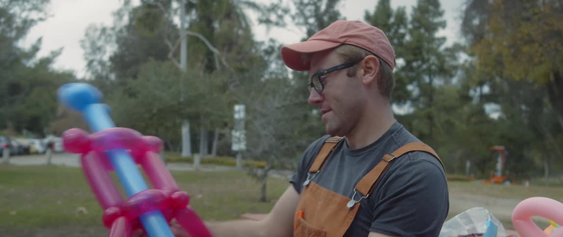 A man making balloon animals outside at a picnic table