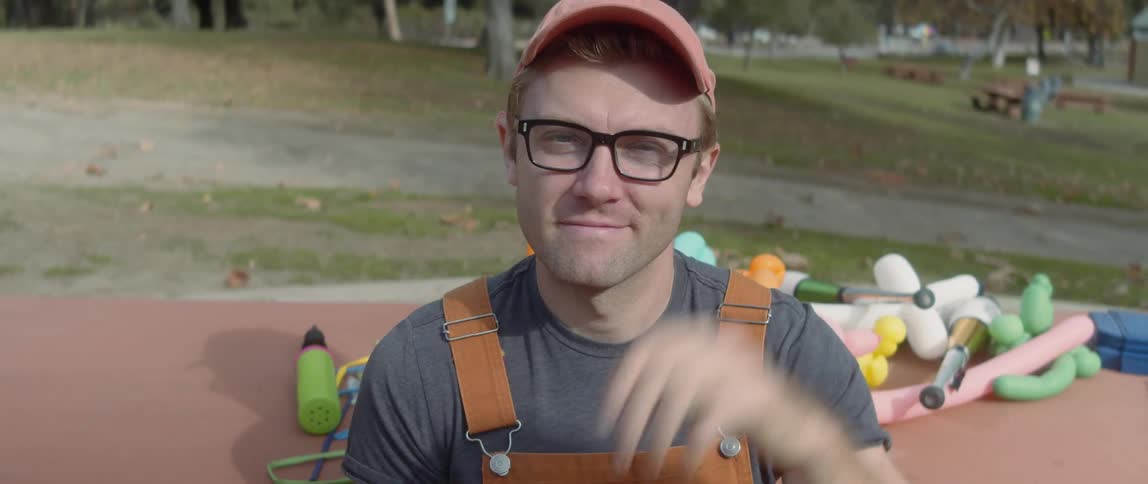 A male balloon artist posing for a portrait outside with baloons in the background