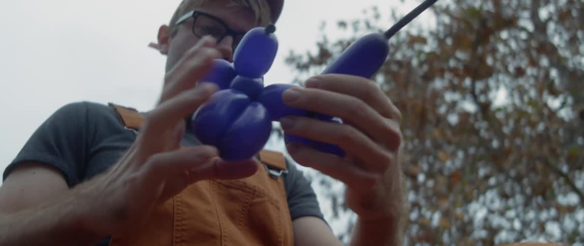 Man wearing overalls makes balloon animals on the park