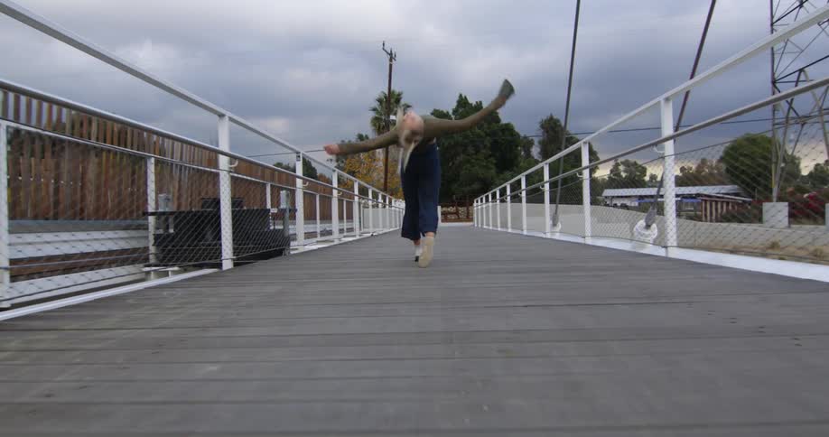 Young performer dances fluidly while running over a suspension bridge