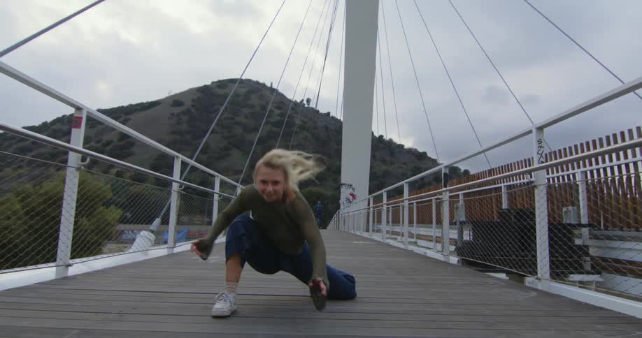 A blonde woman dancing on an outdoor suspension bridge