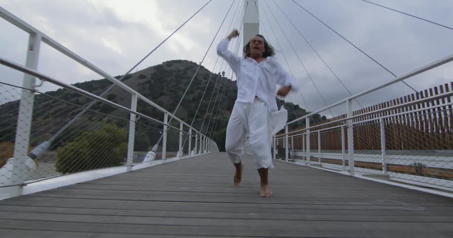 Young performer wearing white clothes dances fluidly over a suspension bridge
