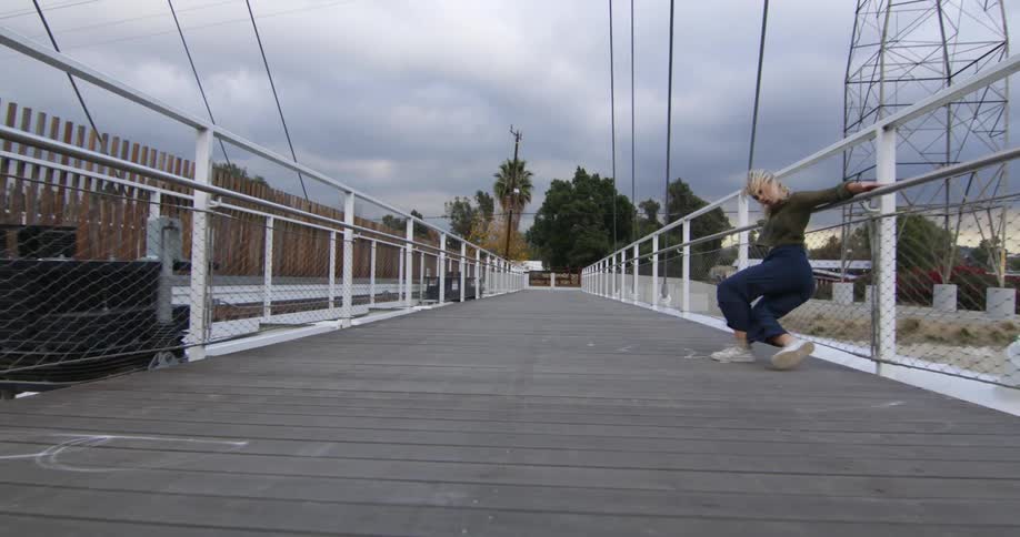 Young performer dances fluidly walking backwards over a suspension bridge