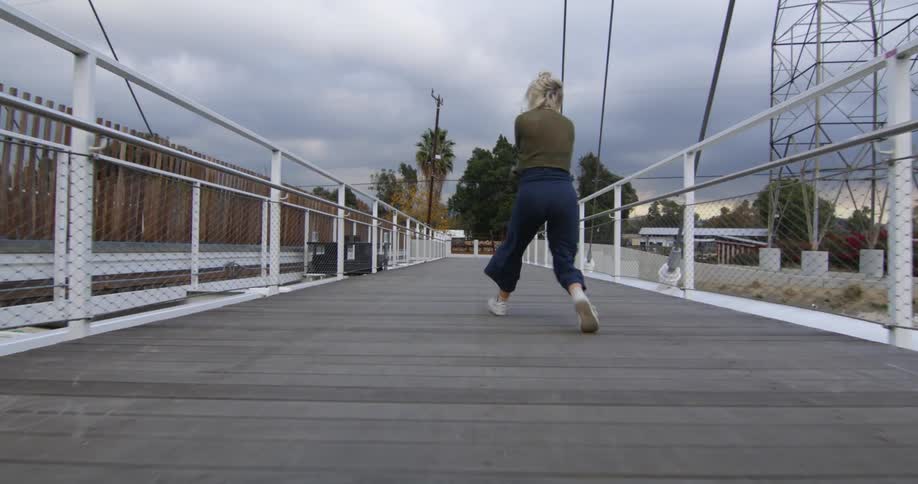 Blonde female dancer dances along pathway near electric transmission tower