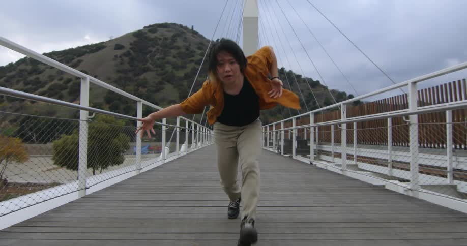 Young performer dances fluidly walking forward over a suspension bridge