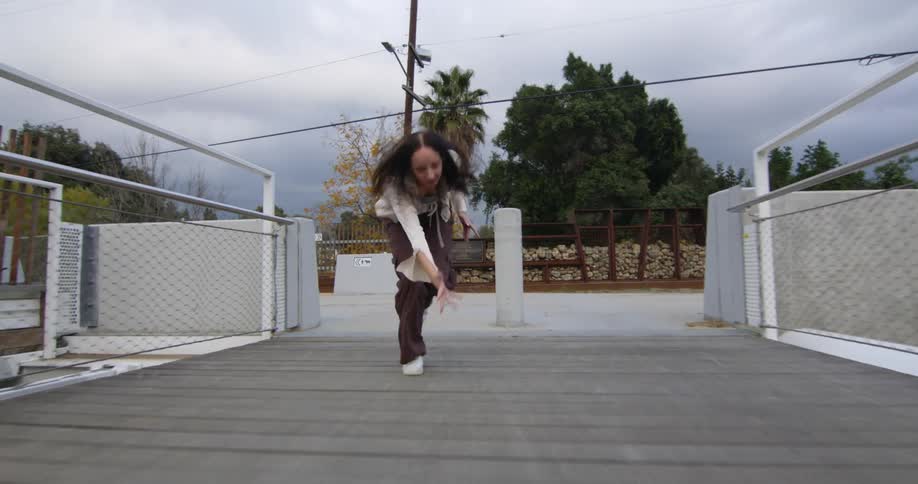 Young woman is dancing backwards on wood plank bridge with a metal railing during the autumn