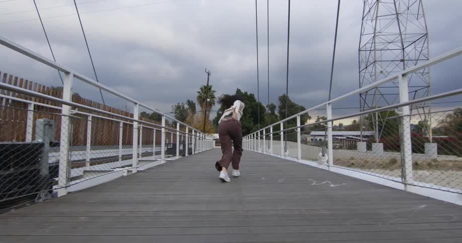 Young performer dances fluidly walking backwards over a suspension bridge